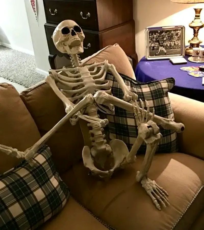 Bộ xương thư giãn trên ghế sofa trong phòng khách, hình nền 1080x1920 HD, phong cách Halloween vui nhộn.