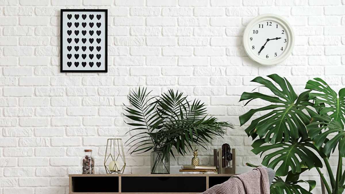 Nội thất phòng khách với tường gạch trắng, cây xanh, tranh nghệ thuật, đồng hồ treo tường. Ảnh HD 1080x1920.